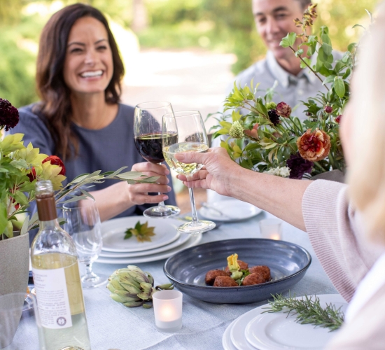 Two women clinking glasses at a dining table decorated with fall foliage.