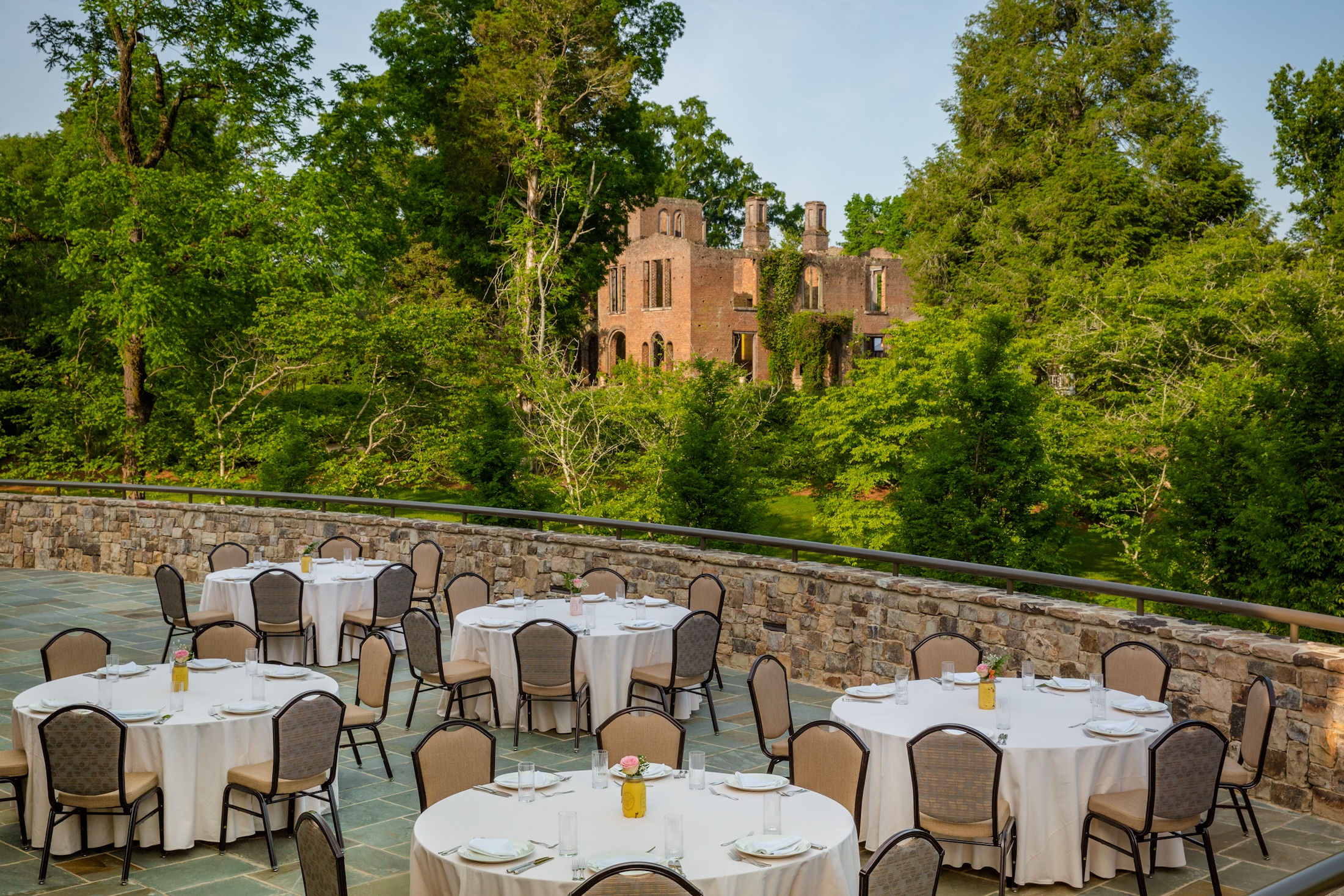 An outdoor seating area with lush greenery and Manor Ruins in the background at Georgian Hall.