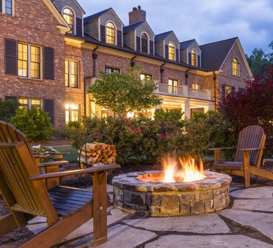 The a fire is lit in an outdoor fire pit in front of a Barnsley Resort inn at dusk.