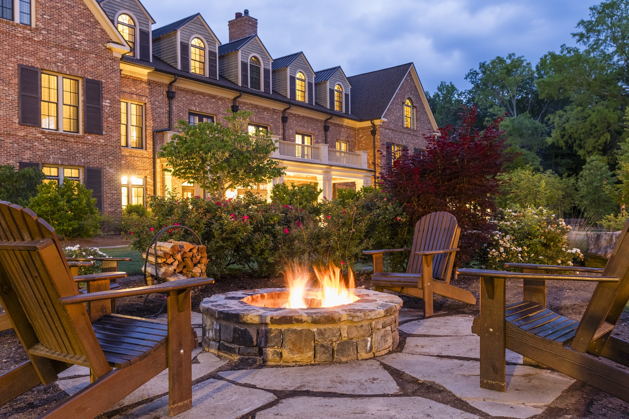 The a fire is lit in an outdoor fire pit in front of a Barnsley Resort inn at dusk.