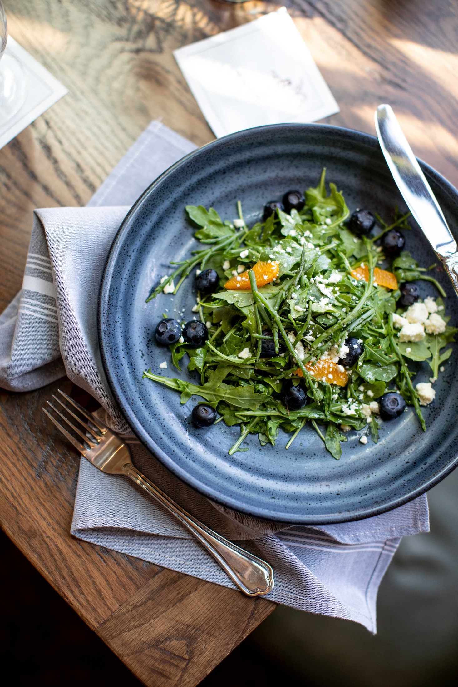 A salad plated on a stone plate with linen napkin on a wooden table.