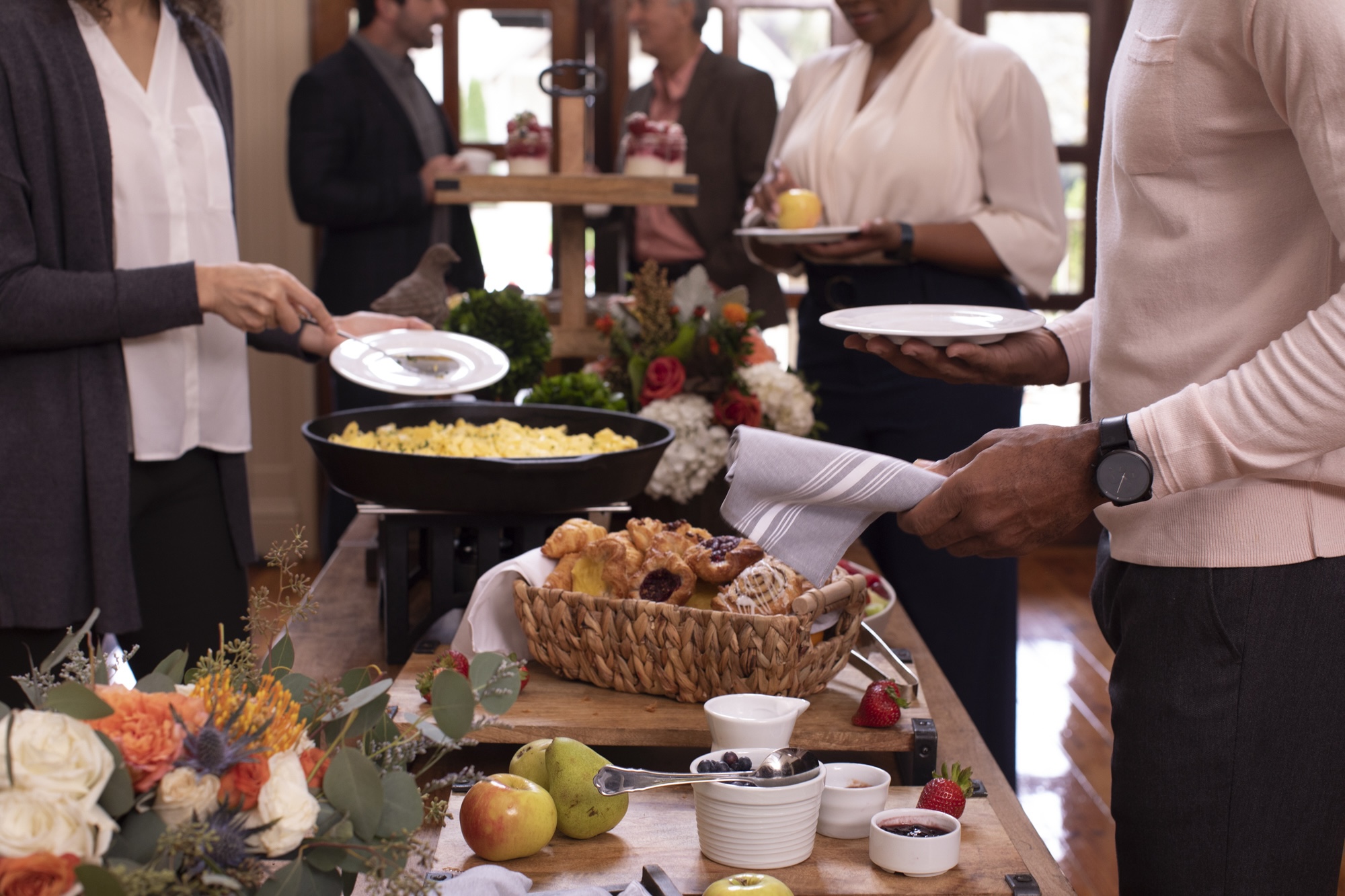 Hotel guests help themselves to breakfast from a buffet table of pastries, fruit, eggs and yogurt parfaits.