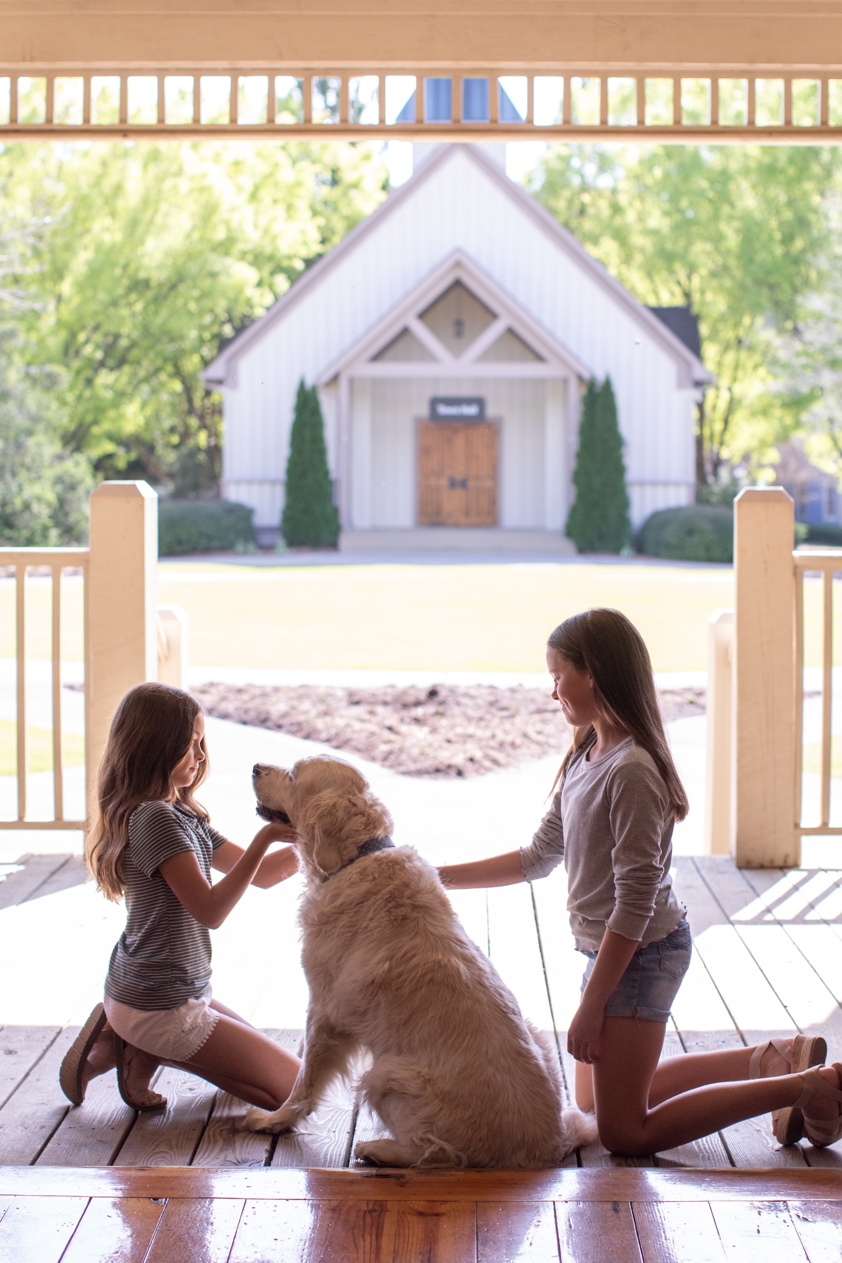 Two young girls petting a golden retriever dog on a covered porch at Barnsley Resort.