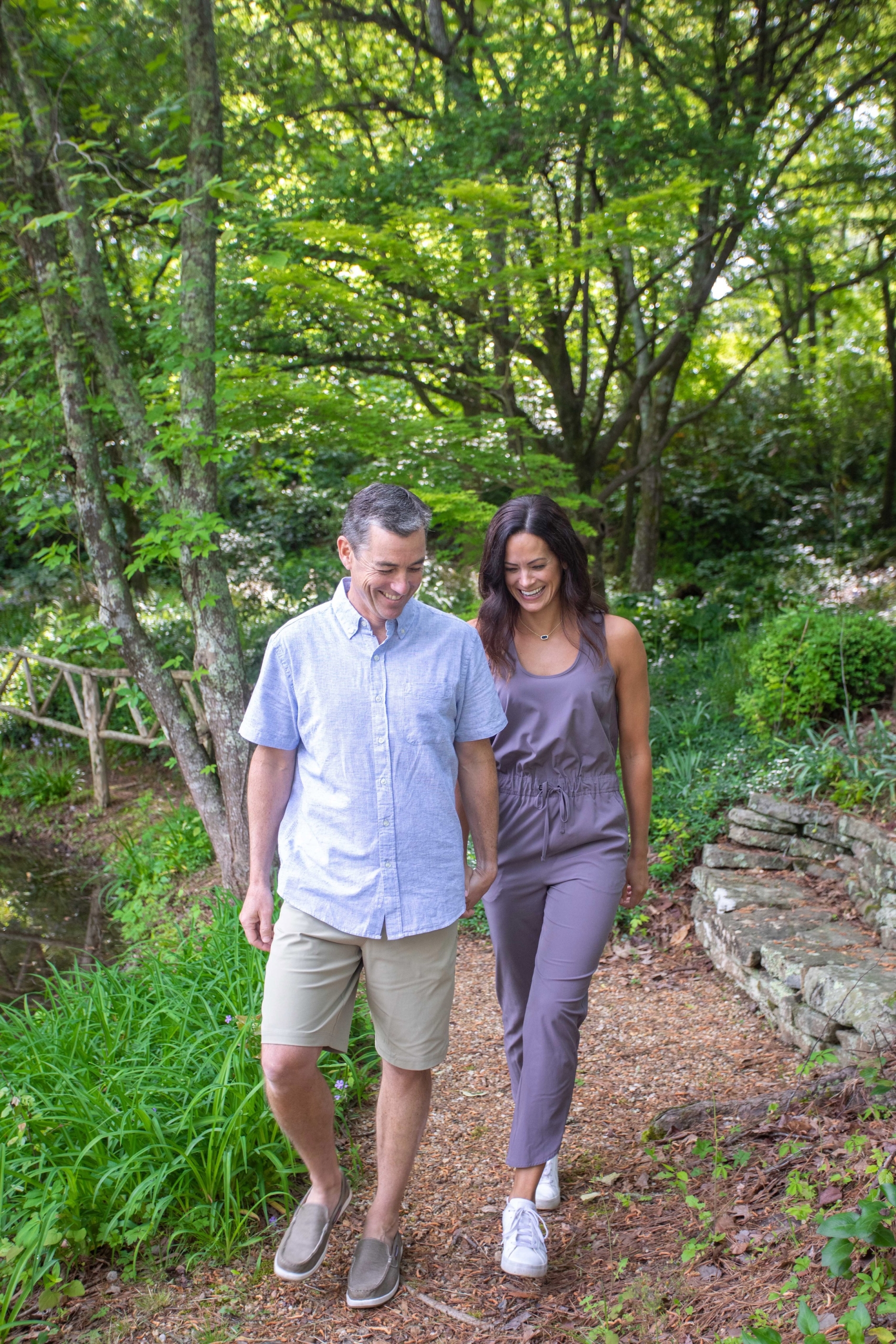 A couple holding hands and walking on a manicured trail on a sunny day.