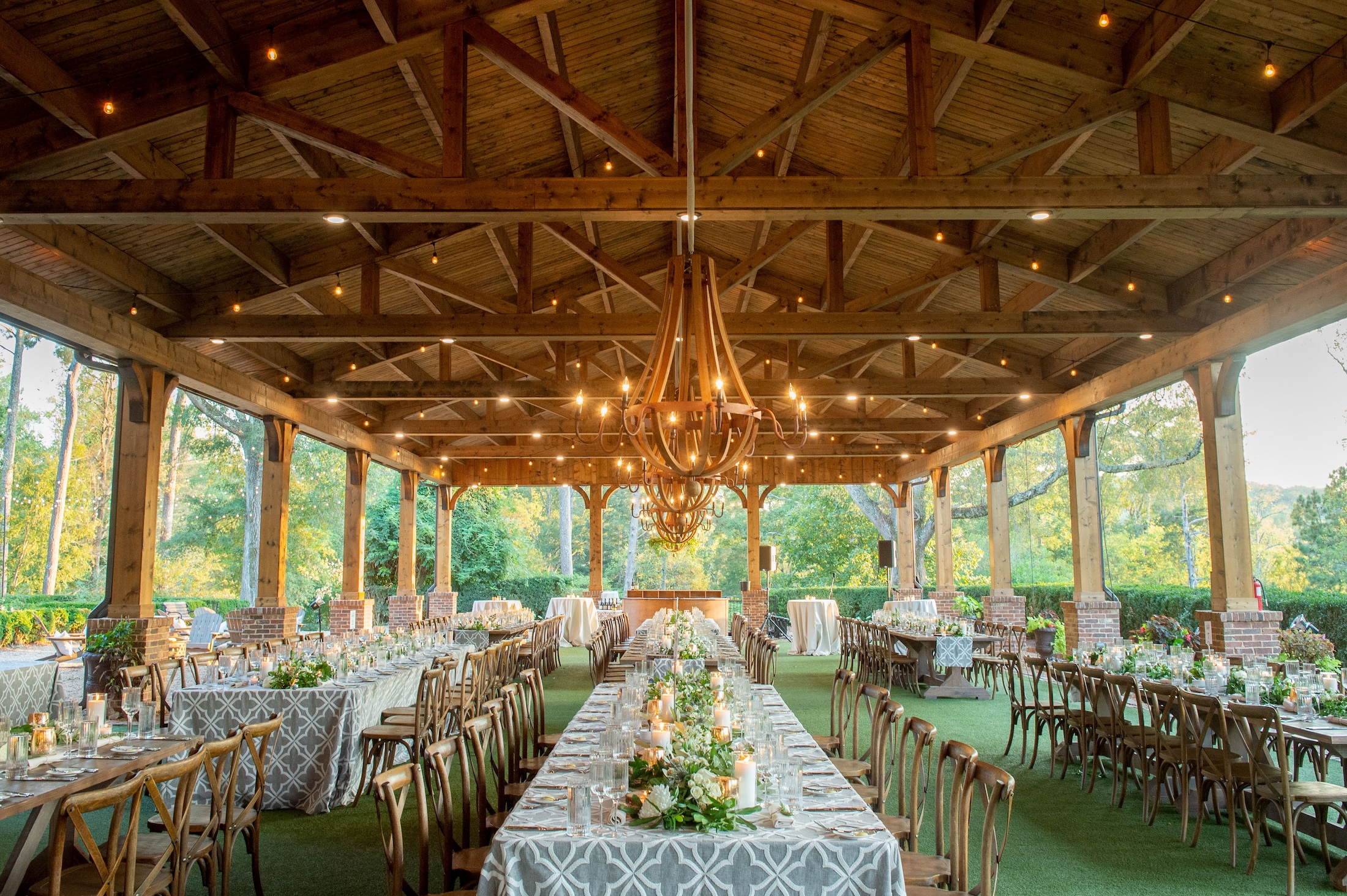 An outdoor wedding venue with long banquet tables set with floral and candle placements.