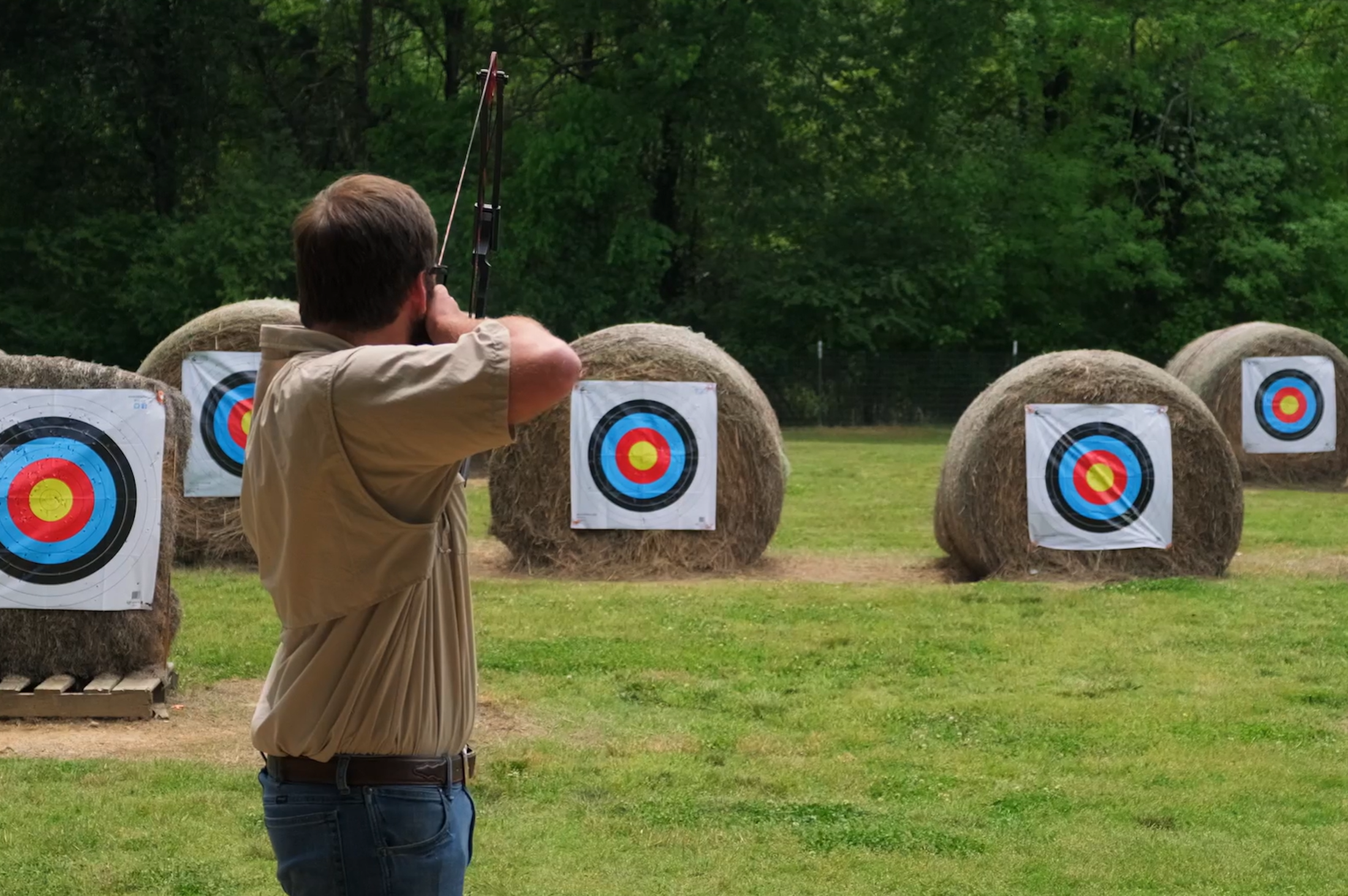 A man shooting an arrow at a target on a hay bale using a bow.