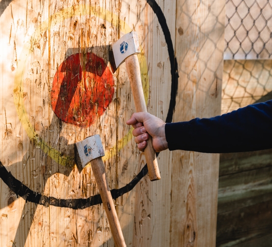 A person removes one of two axes from a painted target on a wooden board.