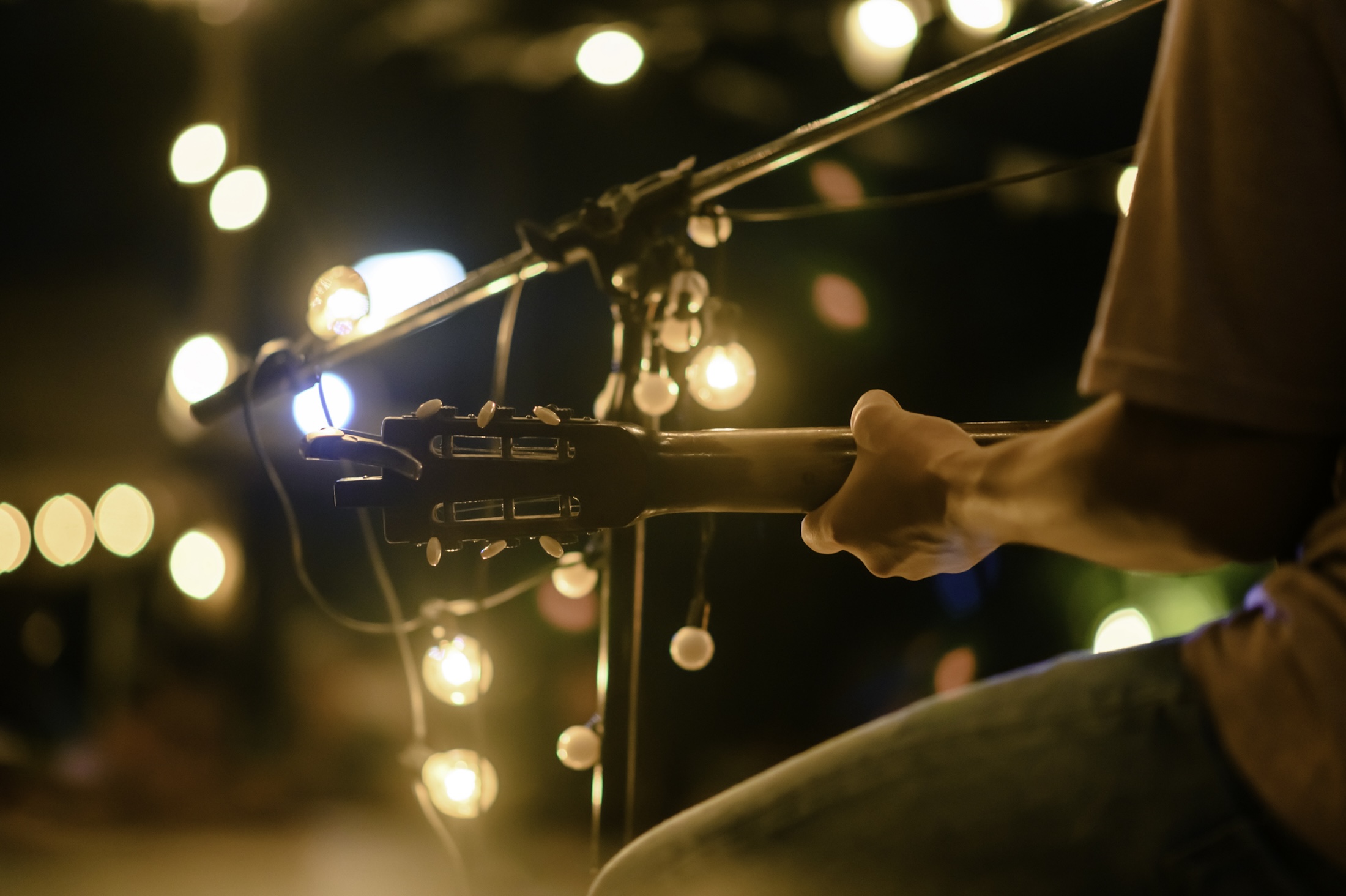 Rear view of the man sitting play acoustic guitar on the outdoor concert with a microphone stand in the front.