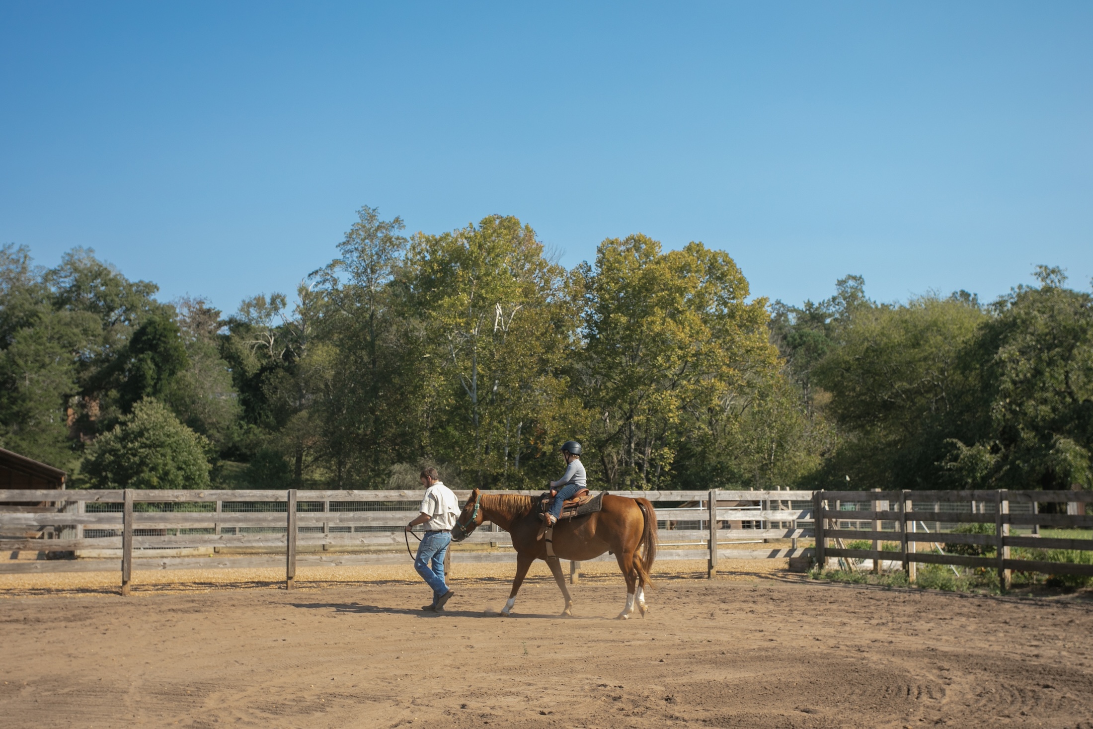 A man leading a horse with a child sitting on it through a fenced in area.