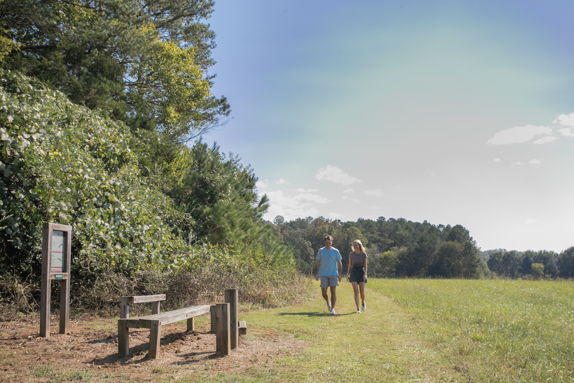 A couple walking up to a trailhead on a manicured stretch of grass.