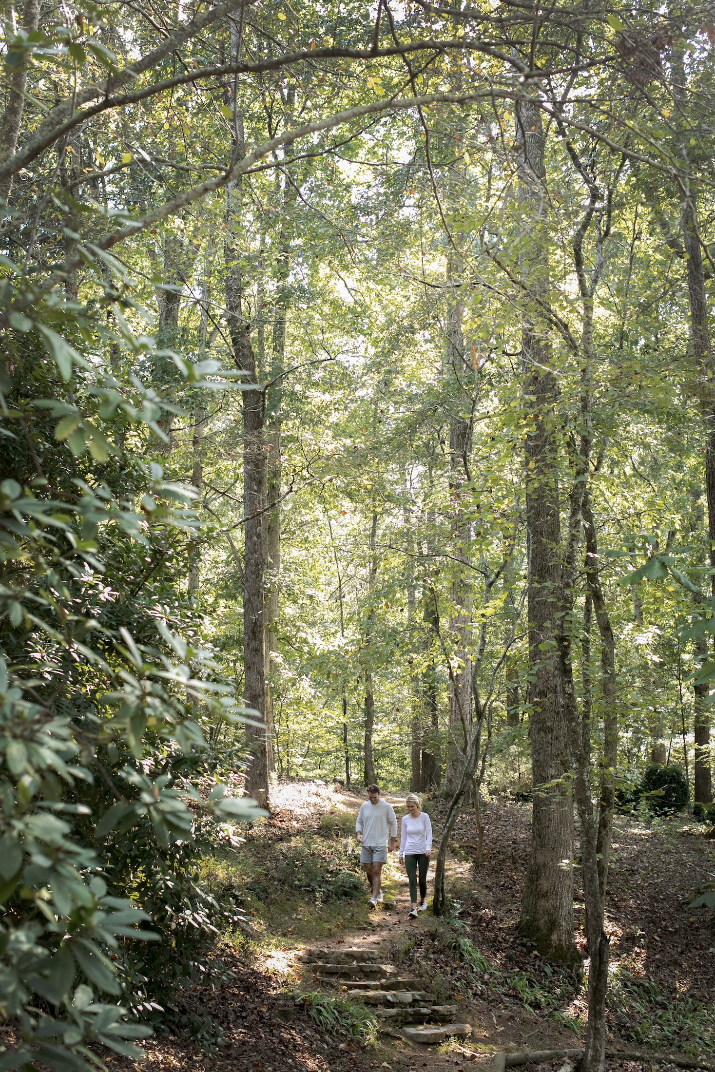 A couple walks through a maintained trail with tall trees on sunny day.