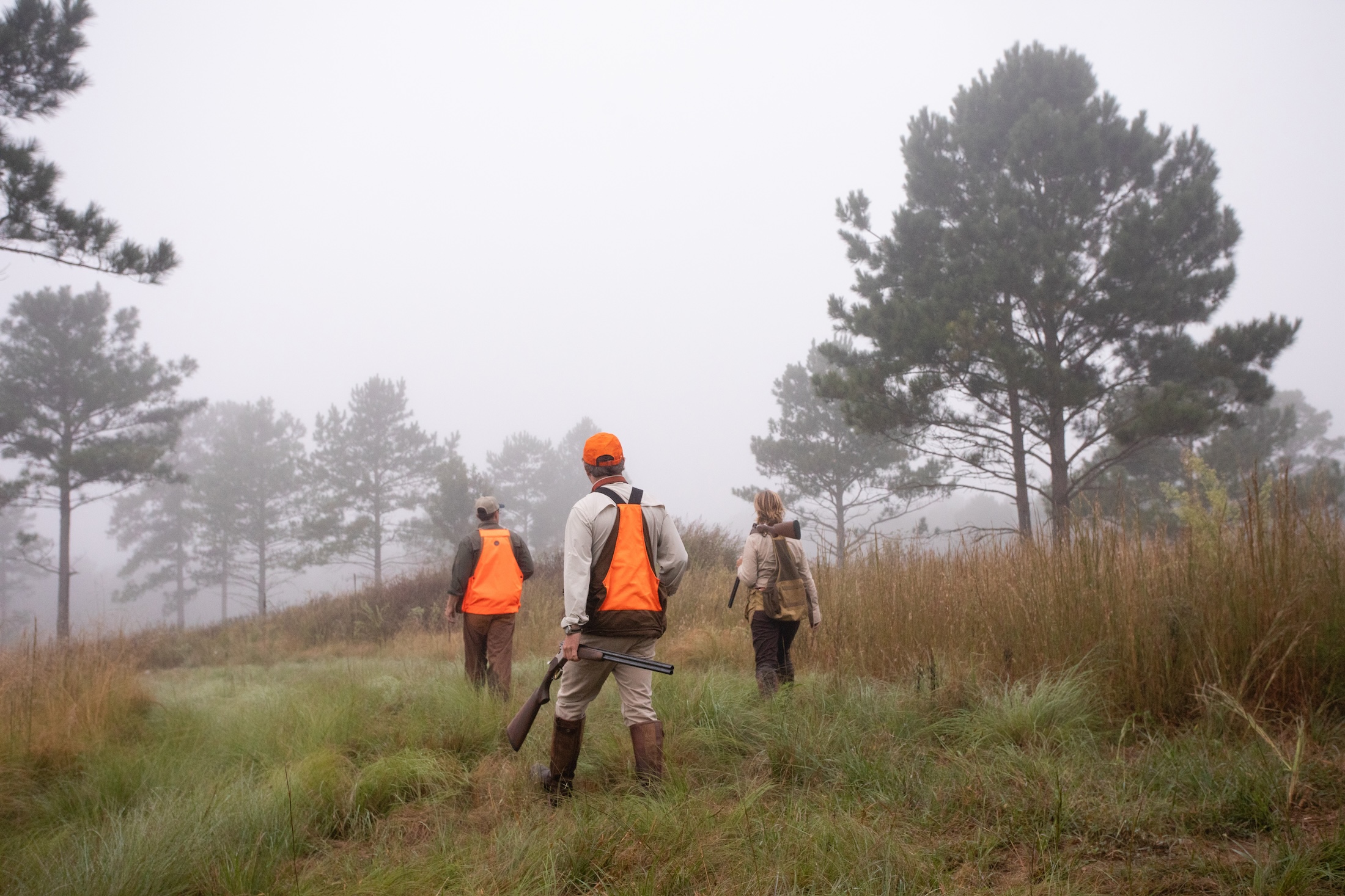 Three people in hunting gear walk through a foggy field lined with trees at the Beretta Shooting Grounds.