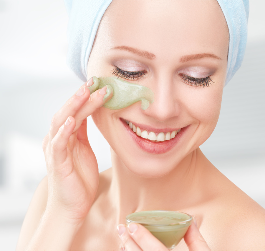 A woman applies a green mask to her face under her eyes in a spa.