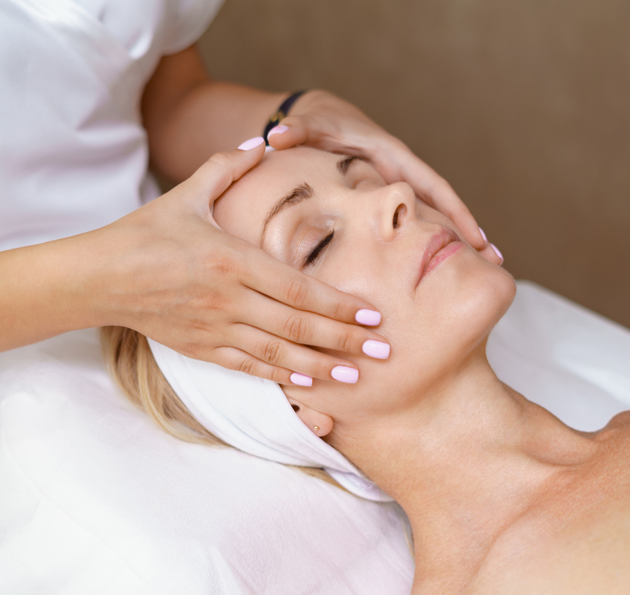 A spa worker gives a woman a light facial massage with both hands.