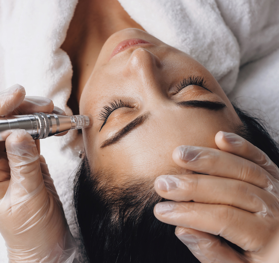 The gloved hands of a spa worker uses a HydraFacial tool under a women's eyes.