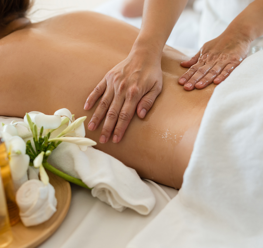 A spa worker uses massage oil on the lower back of a guest during their massage.