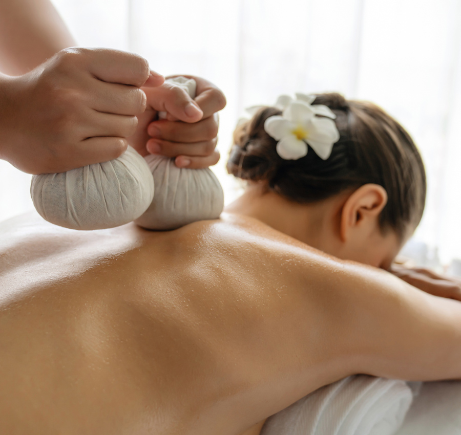 A woman laying down on a massage table receives a herbal massage.