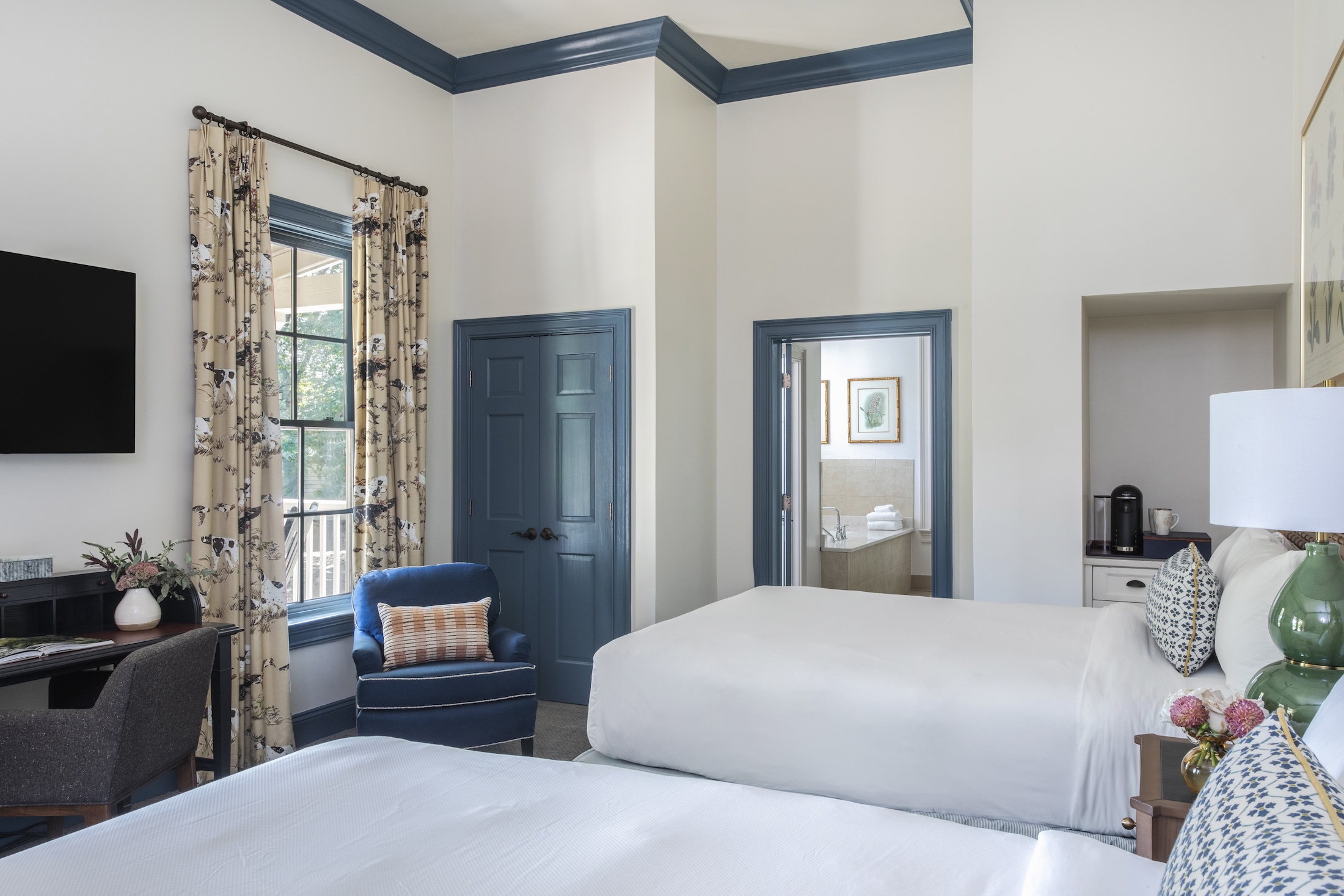 A bedroom suite with two queen beds, a desk, a plush chair and coffee maker.