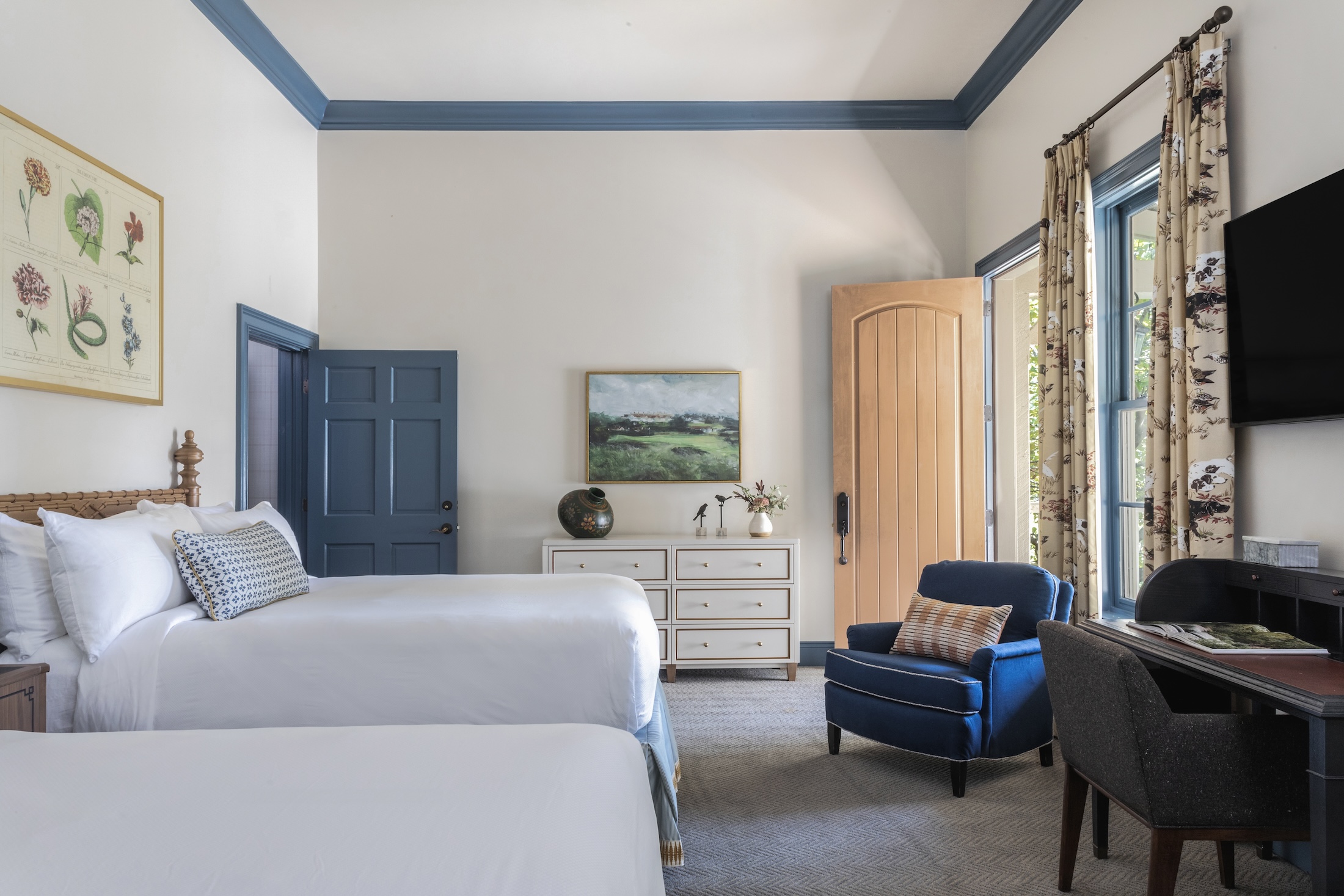 A bedroom suite with two queen beds, a desk and plush chair with a door leading outside.