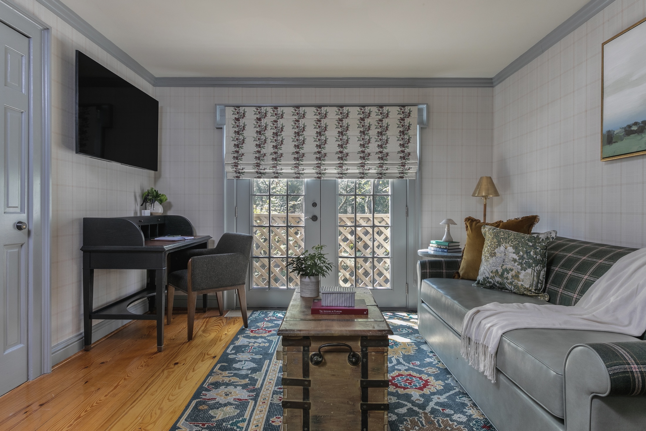 A living room area in Wheaton Cottage featuring light colors, a comfortable sofa, TV and small desk and chair.