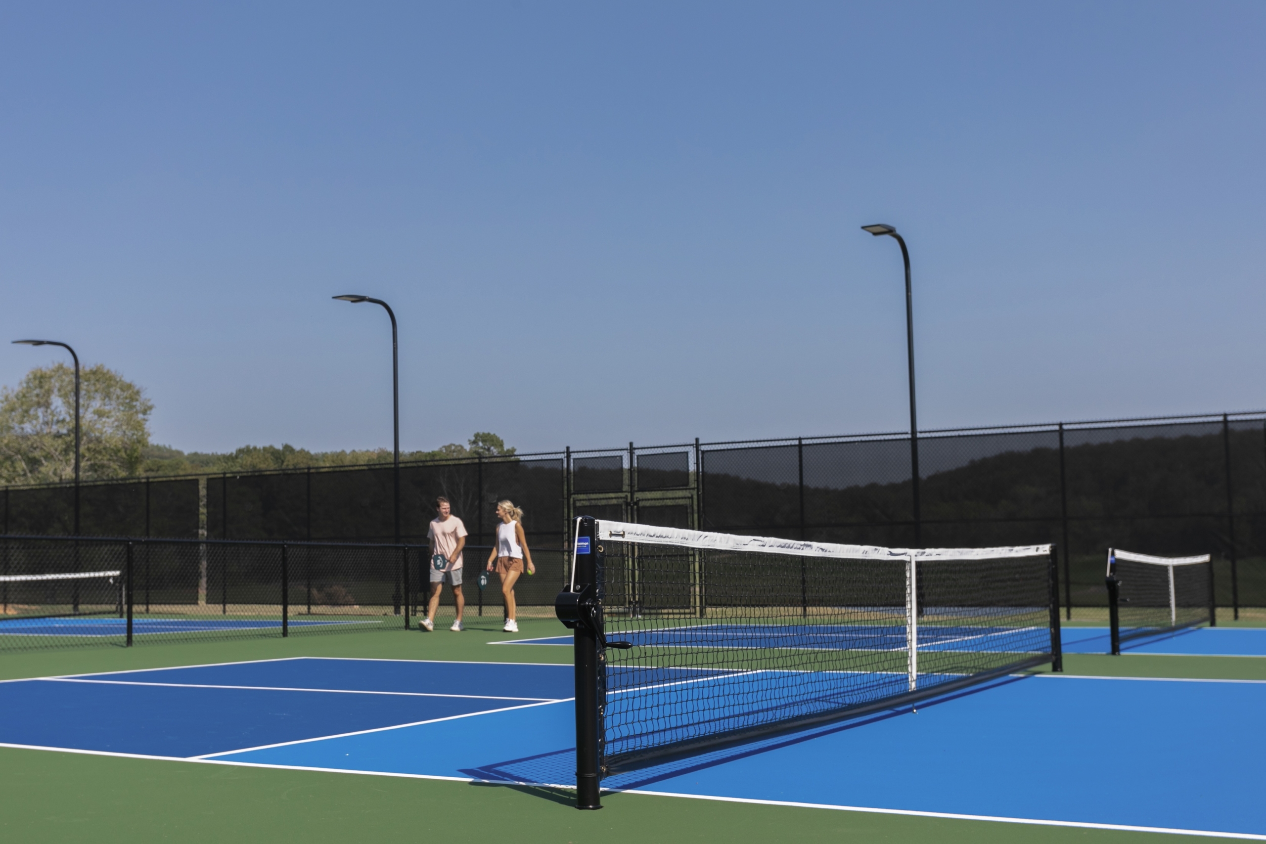 A couple walks through a pickleball court on a sunny day.