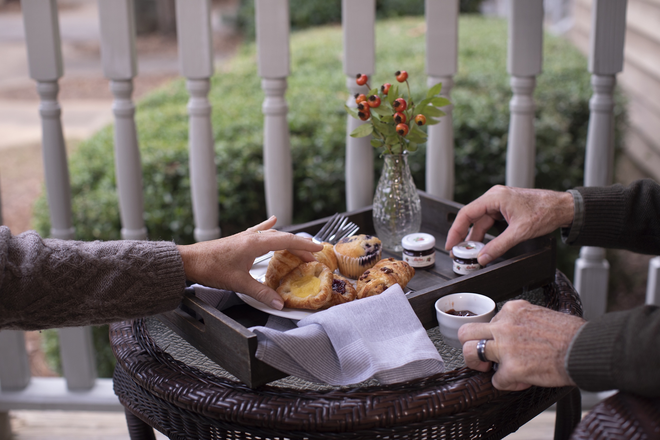 A breakfast pastry tray with assorted jams on a patio table. Two sets of hands are reaching for pasties.