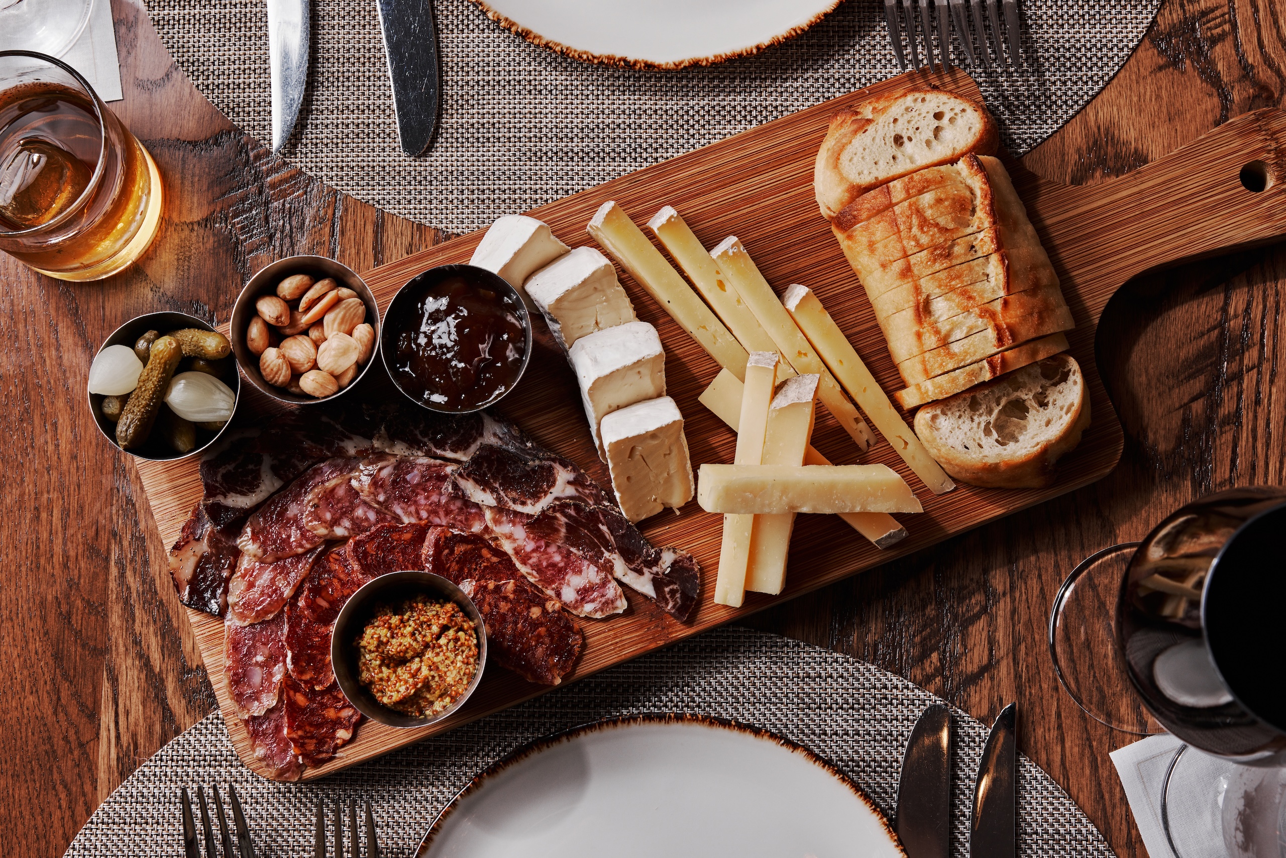 A cheese and charcuterie board of assorted cured meats, cheeses, nuts, pickles, jams and sliced bread.