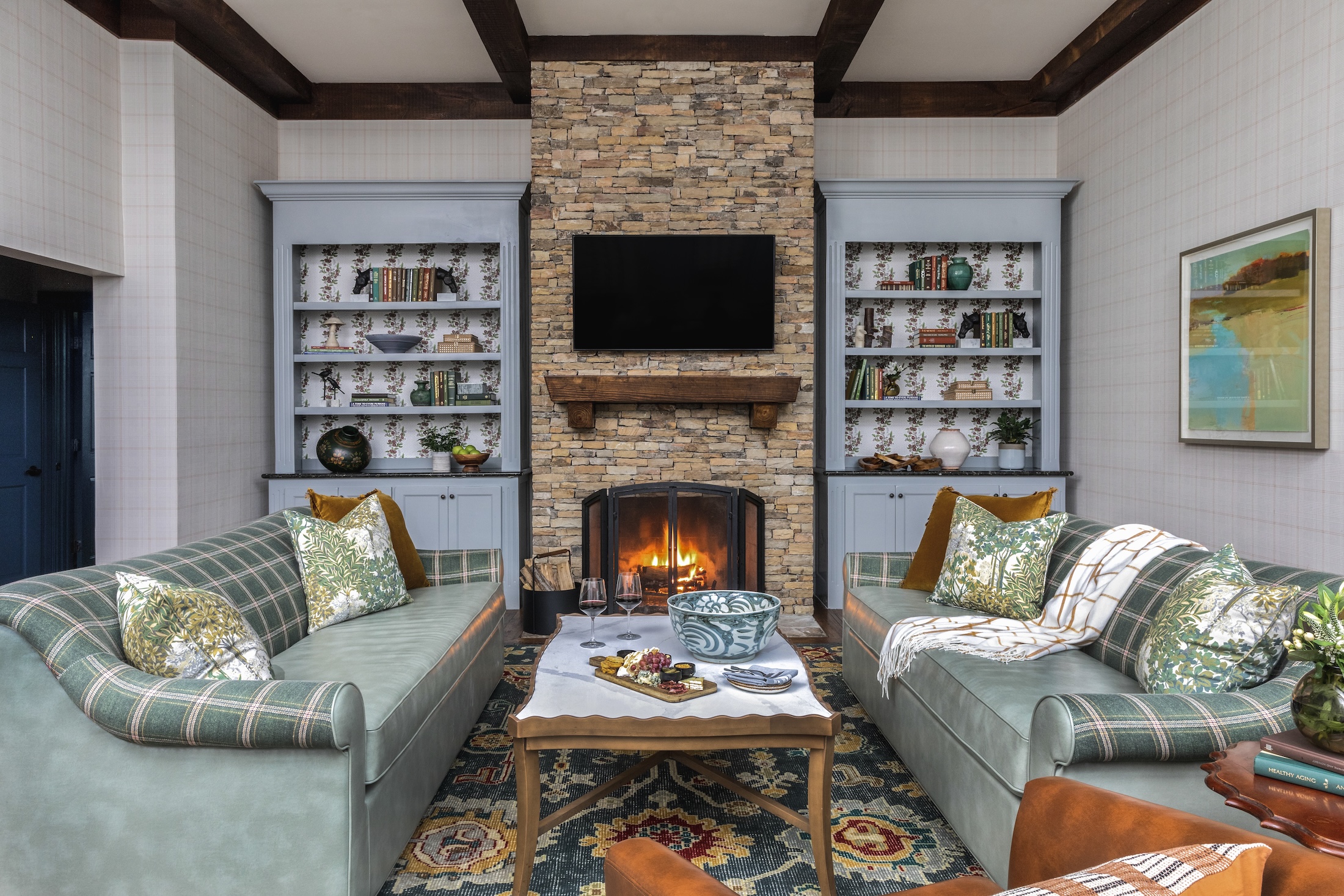 The cozy living room in Godfrey Cottage with a fire in the fireplace. Two couches and an arm chair encircle a table that holds wine and a cheese board.